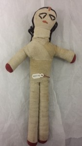 stuffed cloth figure with wrapped strips of cloth forming body and limbs, black cotton thread for hair and stitched thread for facial features.